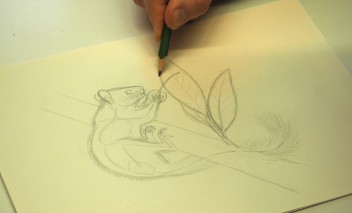 Ręka trzymająca w ręku ołówek i rysująca na kartce mysz. 