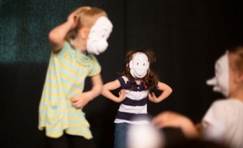 Dzieci w białych maskach na scenie.