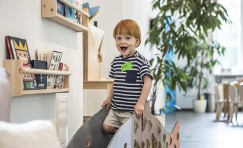 Mały chłopiec bawi się w pokoju z zabawkami na małej zjeżdżalni. 